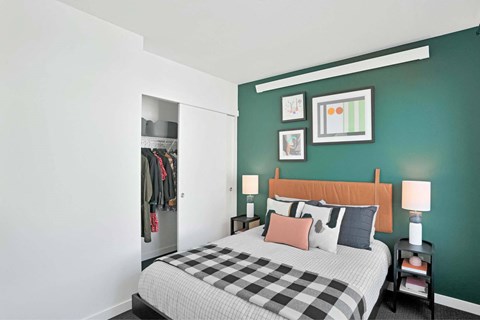A bedroom with a bed, nightstand, and a wall-mounted closet.