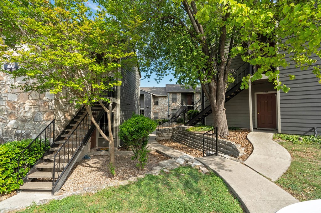 A tree with green leaves stands in front of a grey house.