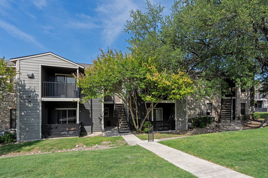 A grey building with a black door and windows is surrounded by trees and grass.