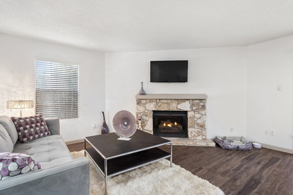 A living room with a grey couch, a black coffee table, a stone fireplace, and a flat screen TV mounted above it.