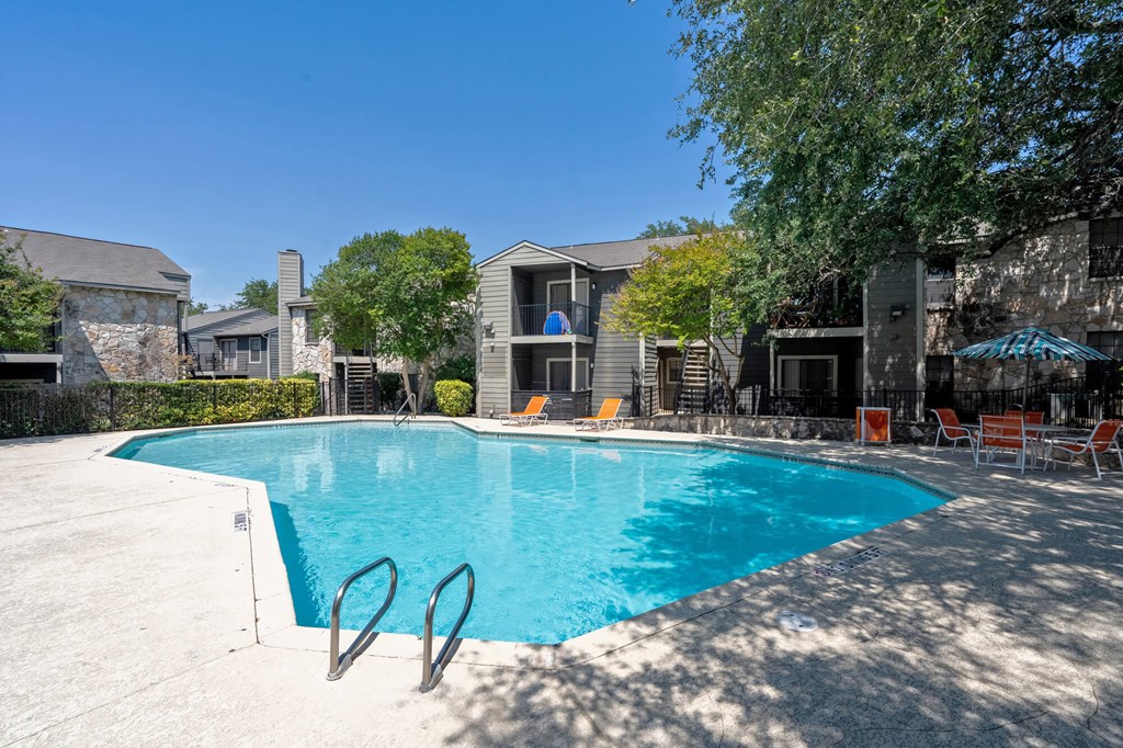 A swimming pool surrounded by chairs and trees.