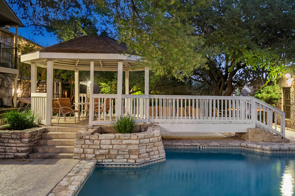A gazebo is surrounded by a pool and stone steps.