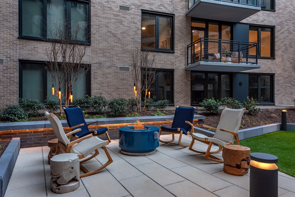 A patio with chairs and a fire pit in front of a brick building.