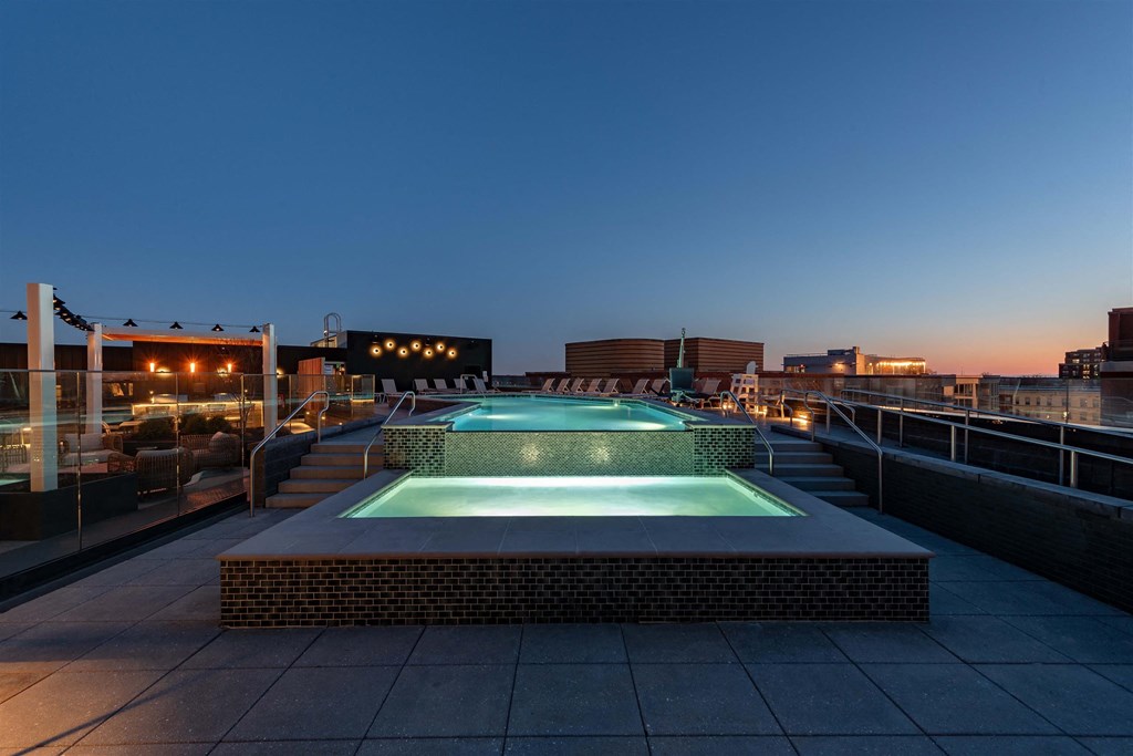 A pool on a rooftop with lights on in the background.
