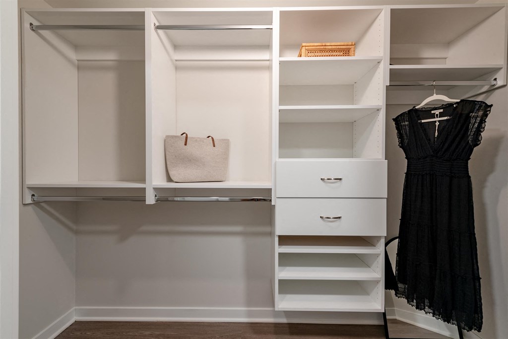 A black dress is hanging on a hanger in a white closet.