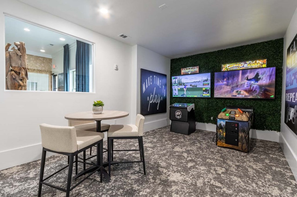 A room with a table, chairs, and a wall of screens showing video games.