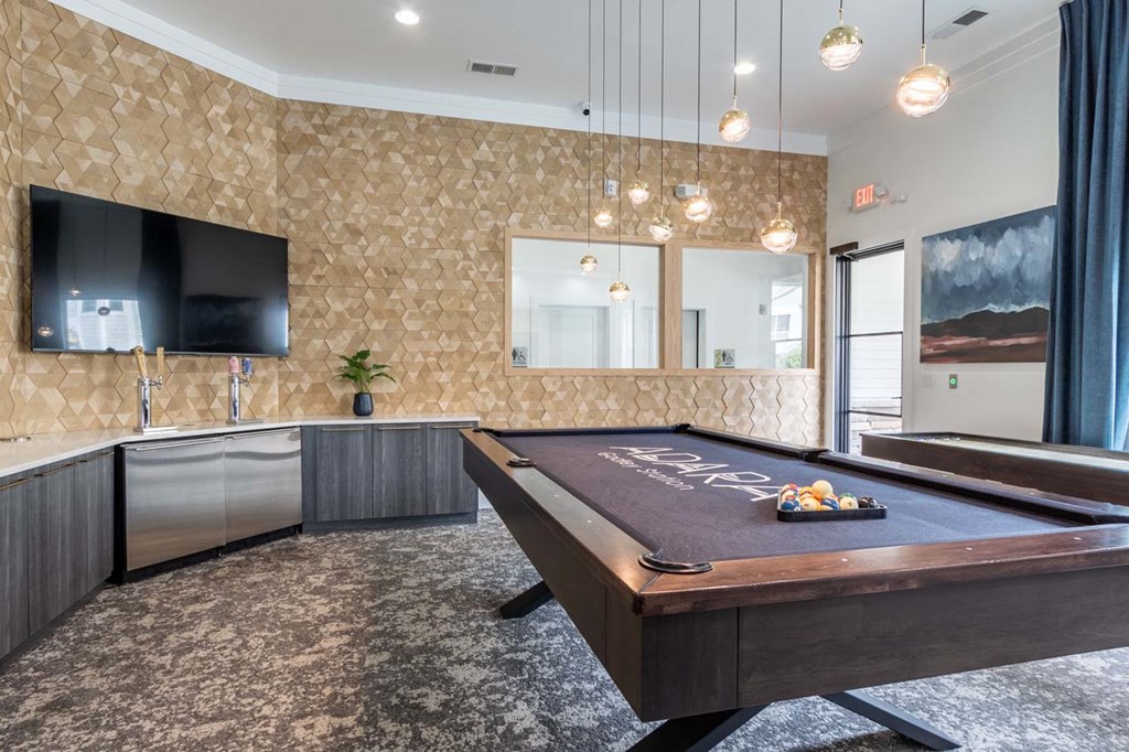A pool table is in the middle of a room with a television and a wallpapered wall.