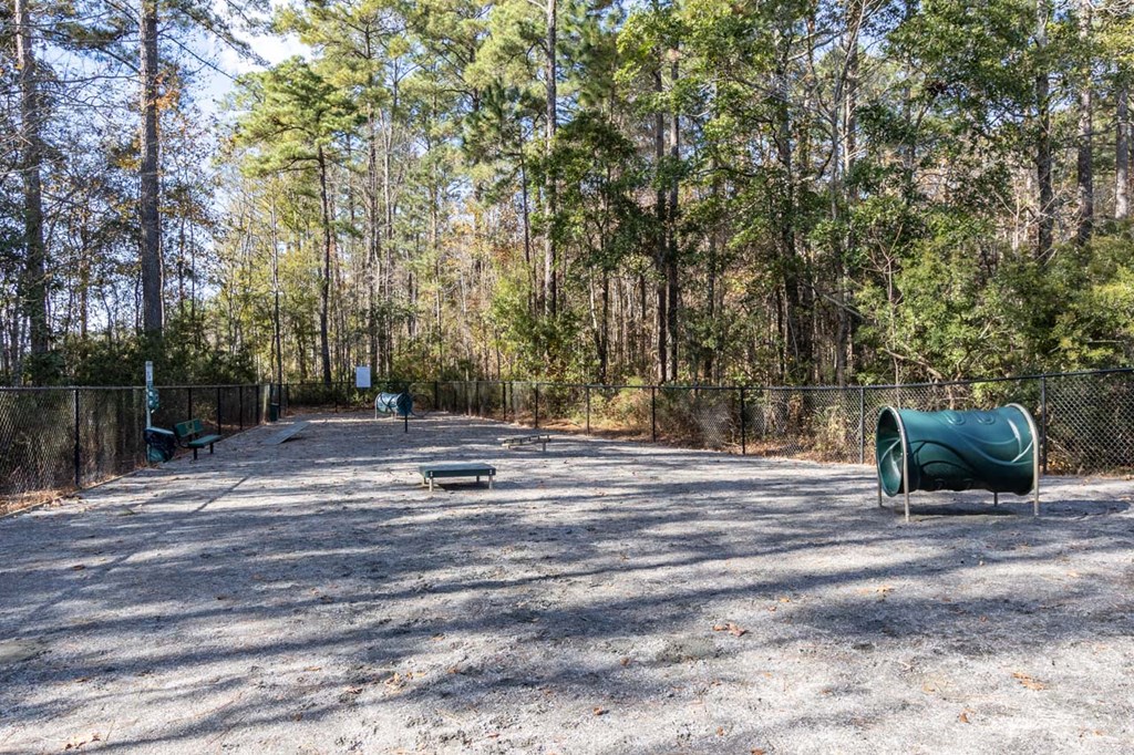 A playground with a green barrel and a slide in a wooded area.