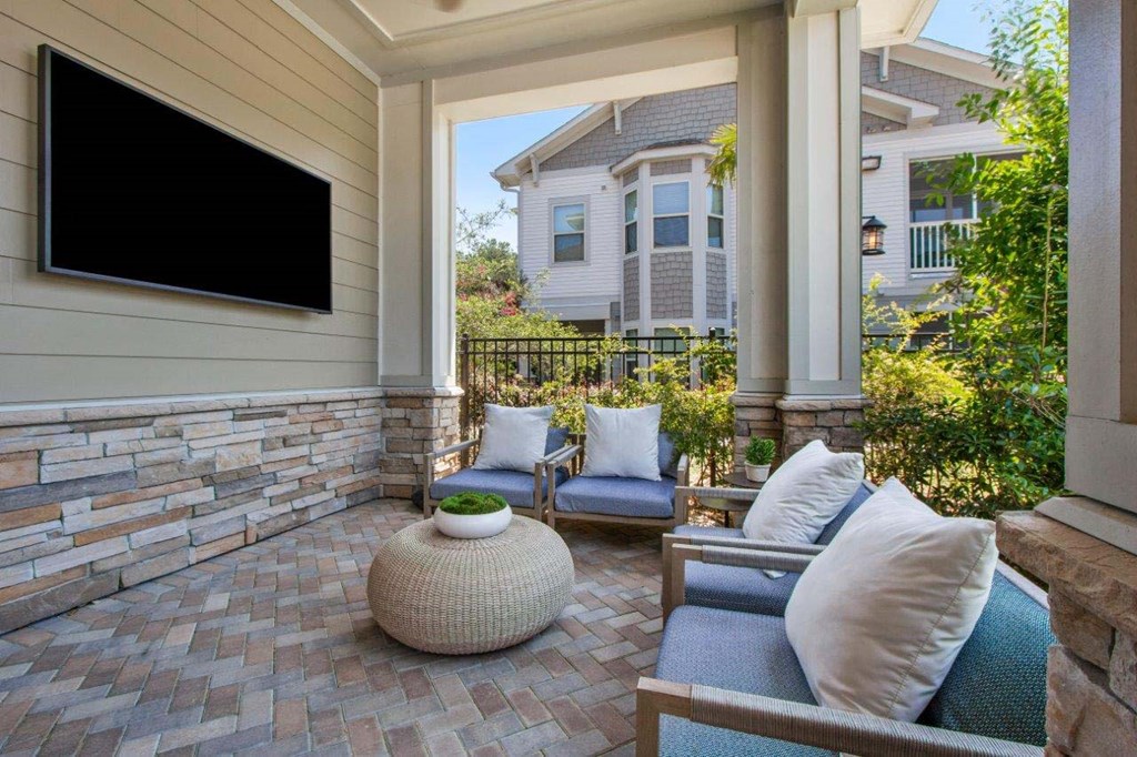 A patio with a couch, chairs, and a television on the wall.