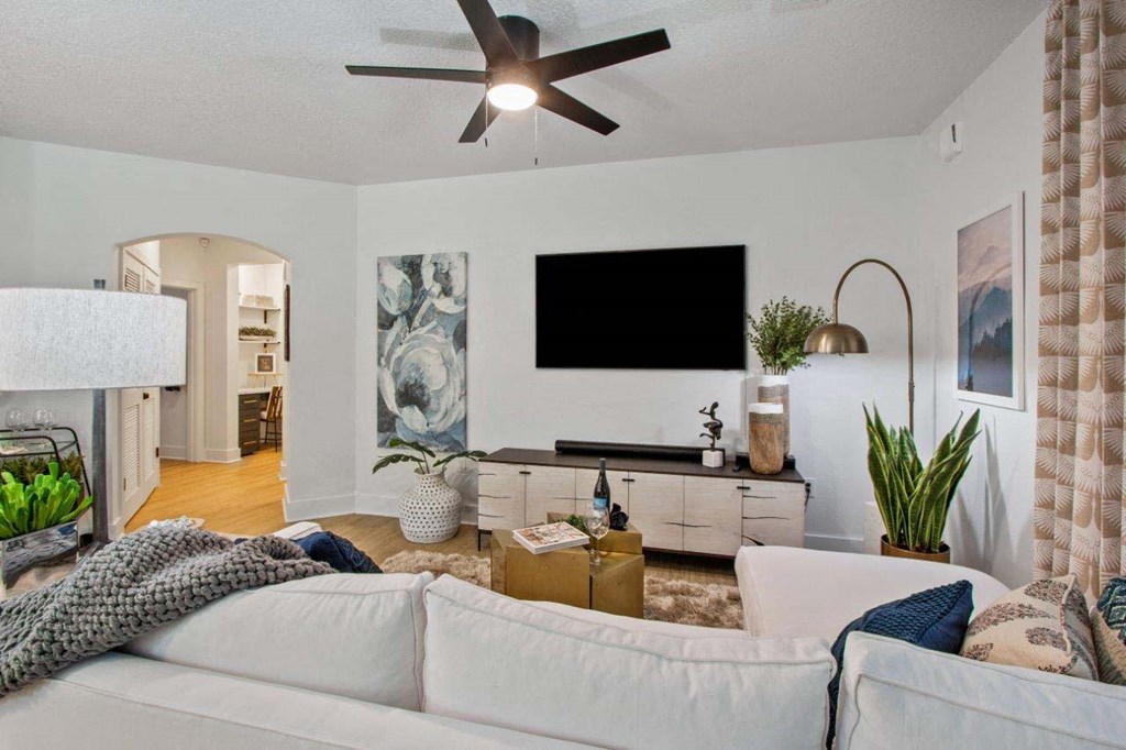 A living room with a white couch and a flat screen TV mounted on the wall.