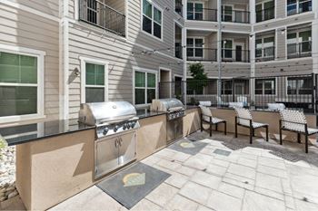 A patio area with a grill and chairs is surrounded by apartment buildings.