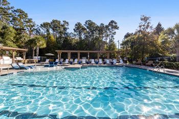 A large swimming pool with sun loungers and a pavilion in the background.