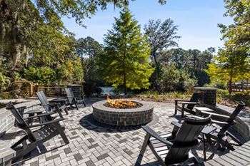 A fire pit in the middle of a brick patio surrounded by chairs.