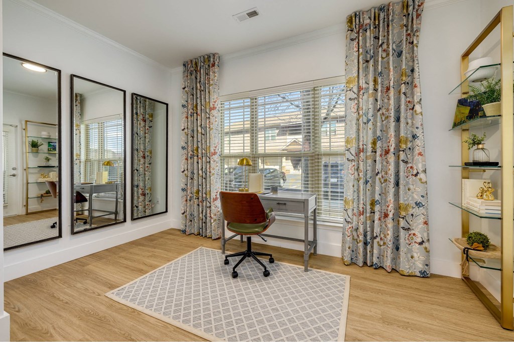 A room with a desk and a chair in front of a window with curtains.