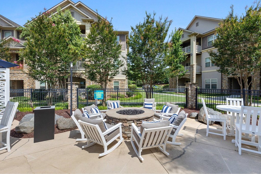 A patio with white chairs and a fire pit in front of apartment buildings.
