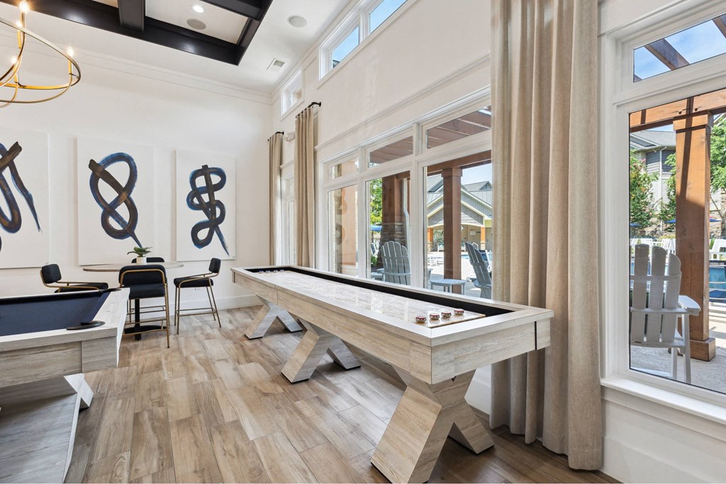 A pool table is in the middle of a room with a wooden floor and a window.