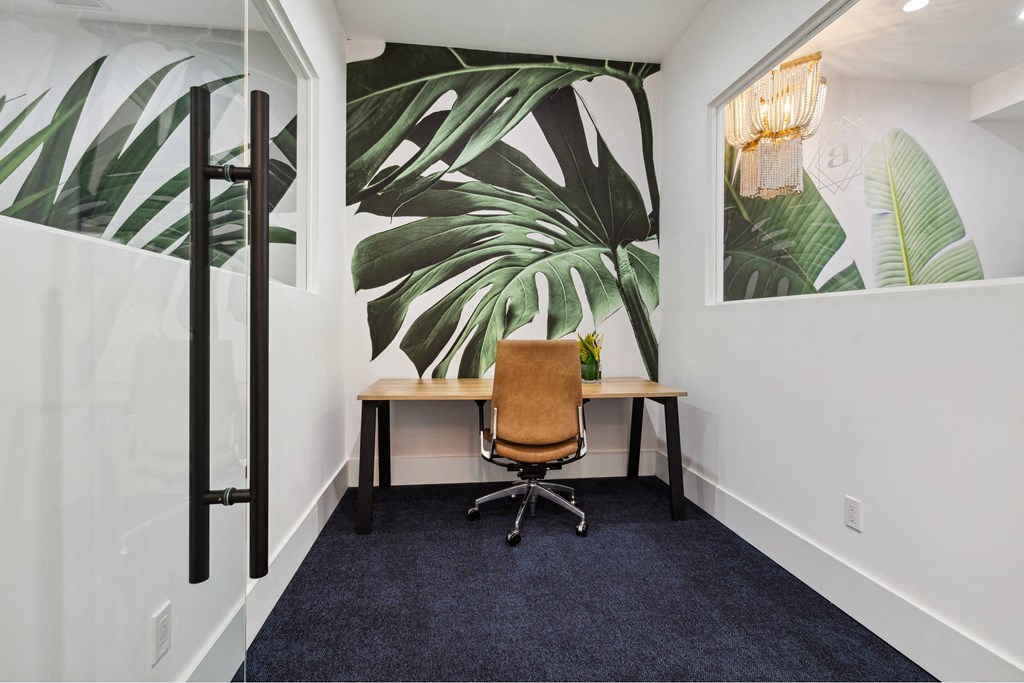 A room with a desk and a chair with a leafy wallpaper.