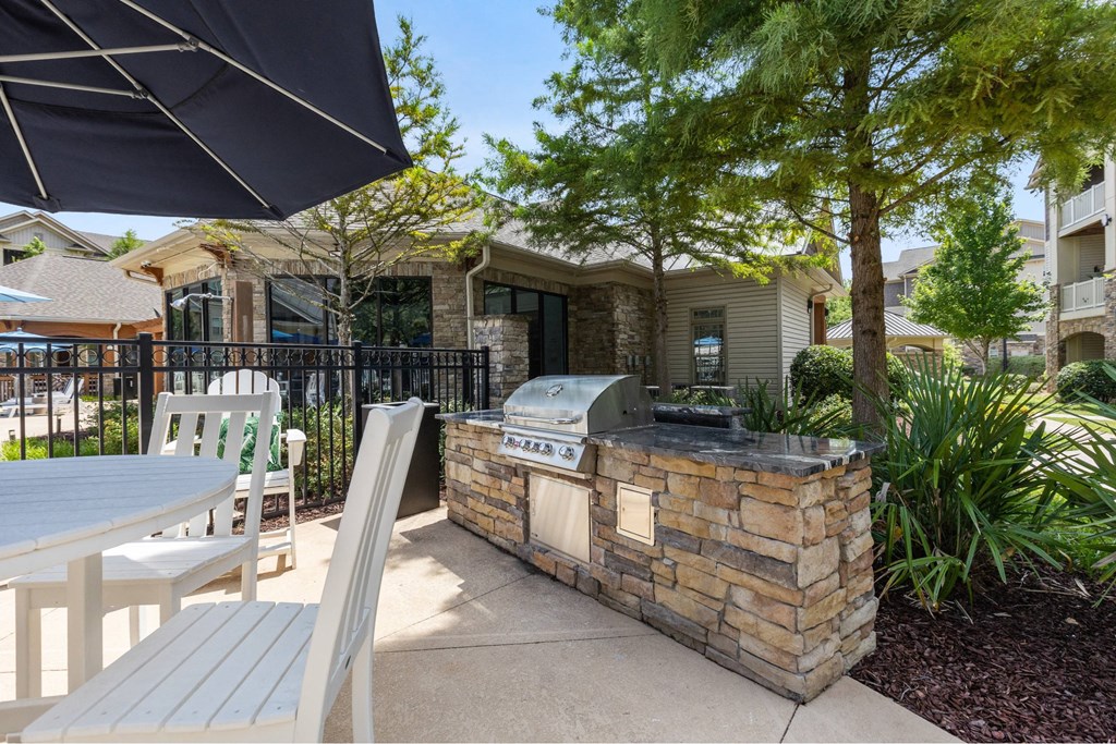 A patio with a grill and chairs under a black umbrella.