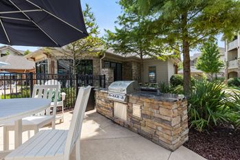 A patio with a grill and chairs under an umbrella.