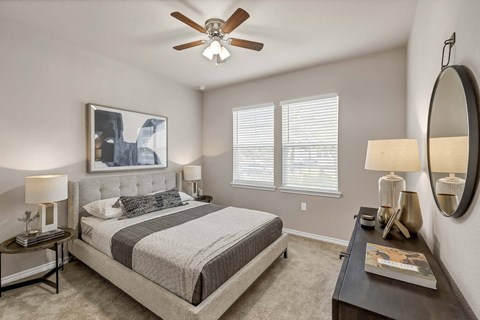 A bedroom with a large bed, a ceiling fan, and a painting on the wall.