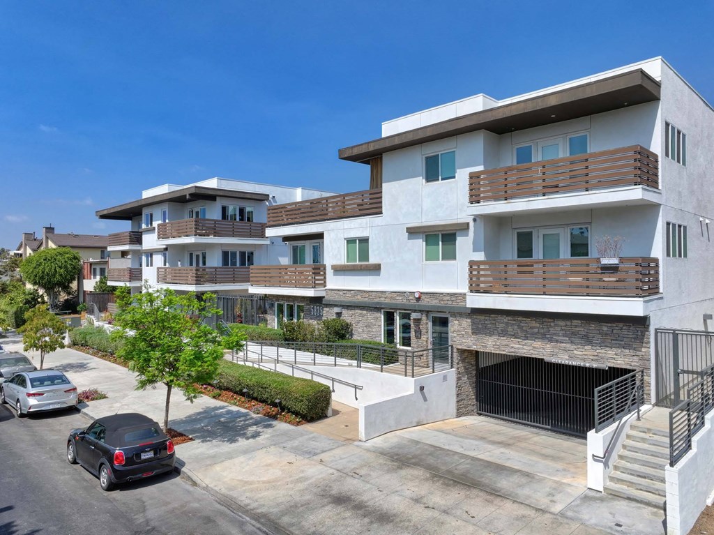 A modern multi-story residential building with a parking area in front.