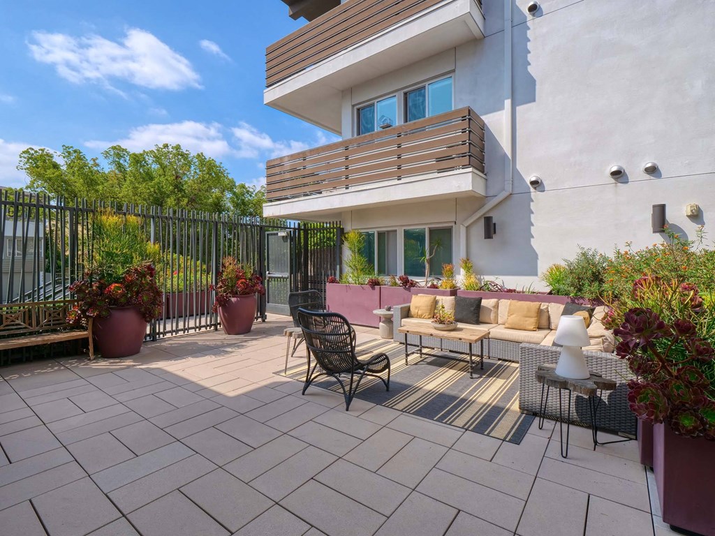 A patio with a black metal chair and a white chair with a cushion, a table and a potted plant.
