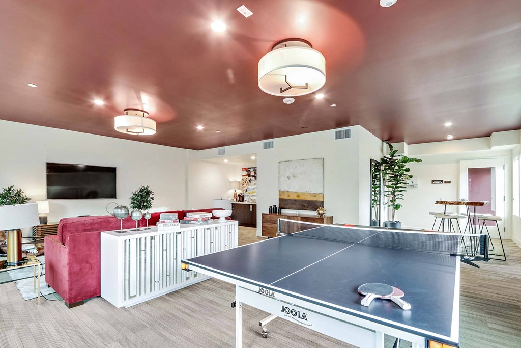 A ping pong table is in the middle of a room with a red couch and a TV.