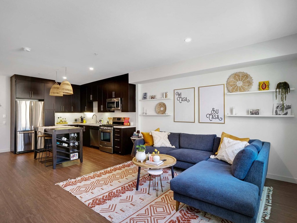 A modern living room with a blue sofa and a kitchen area in the background.
