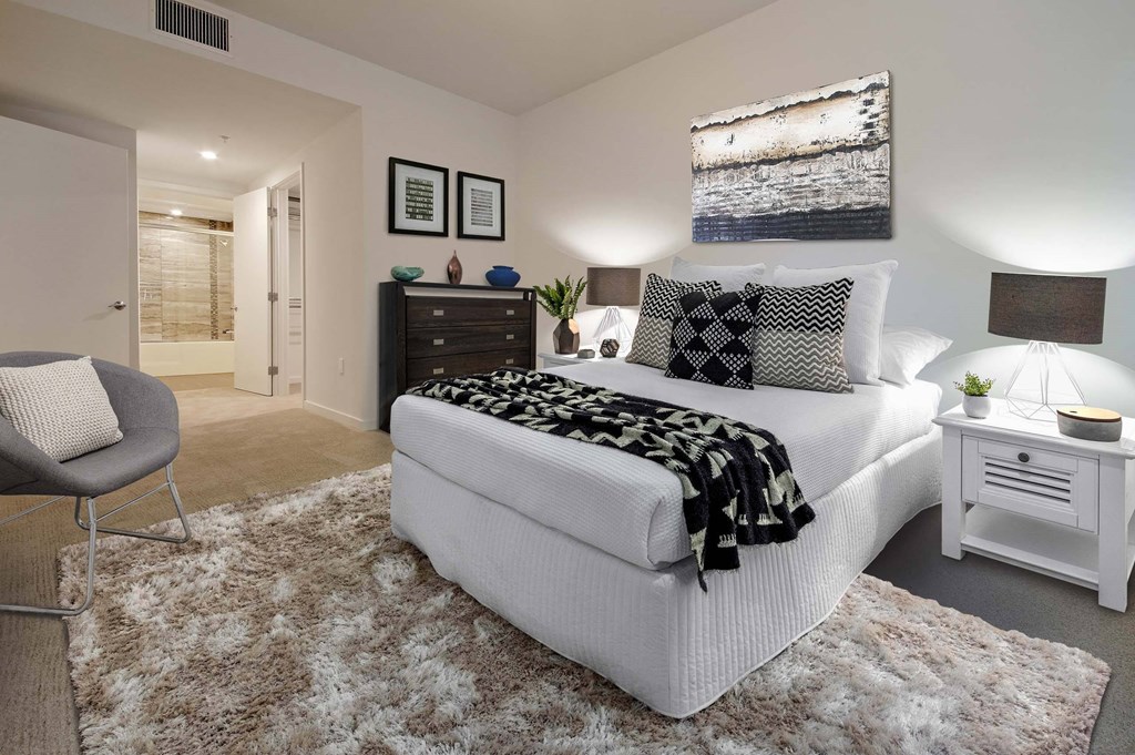 A bedroom with a white bed and a grey chair.