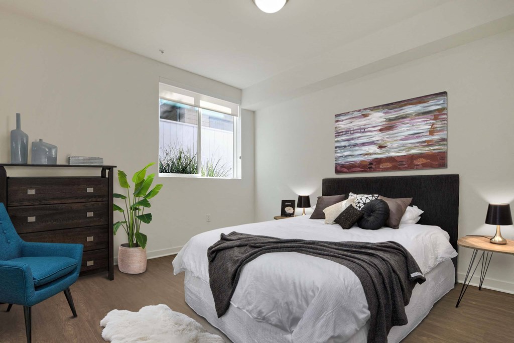 A bedroom with a large bed, a blue chair, and a painting on the wall.