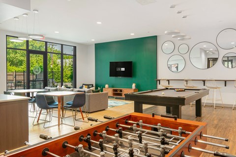 A foosball table is in the middle of a room with a pool table and a television.