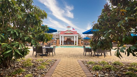 A patio with a table and chairs is surrounded by green plants.