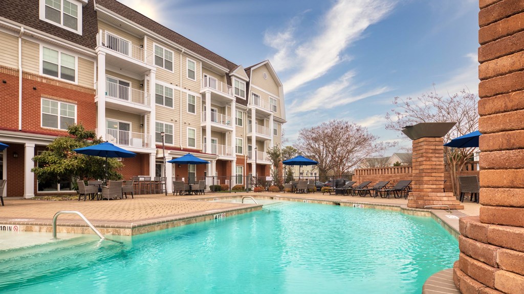 A large swimming pool is surrounded by a brick wall and apartment buildings.