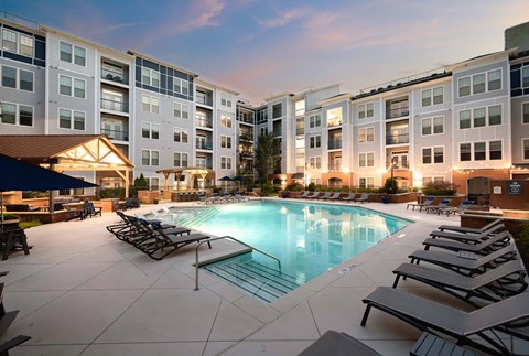 A swimming pool surrounded by lounge chairs in front of apartment buildings.