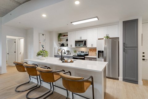 A modern kitchen with a white countertop and brown chairs.