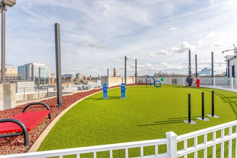 A white fence surrounds a green area with a red bench and blue trash cans.