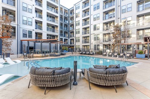A pool area with two wicker chairs and a table in front of apartment buildings.