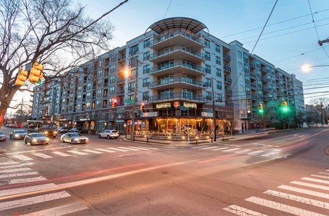 A street view of a city intersection with cars and a large building in the background.