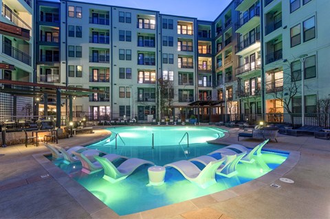 A swimming pool in front of apartment buildings at dusk.