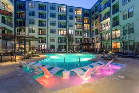 A swimming pool in front of apartment buildings at dusk.