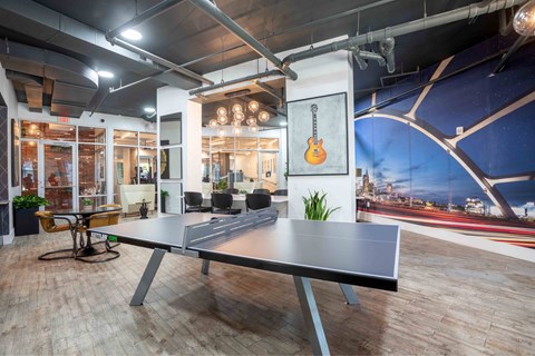 A ping pong table is in the middle of a room with a guitar hanging on the wall.