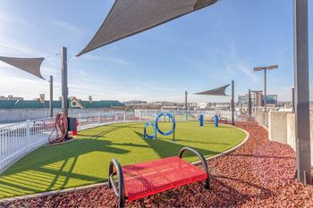 A red bench sits on a grassy area with a playground in the background.