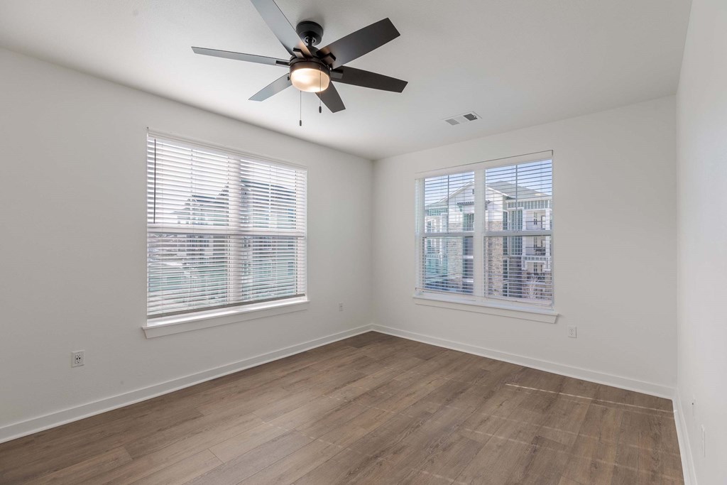 A room with a ceiling fan and two windows.