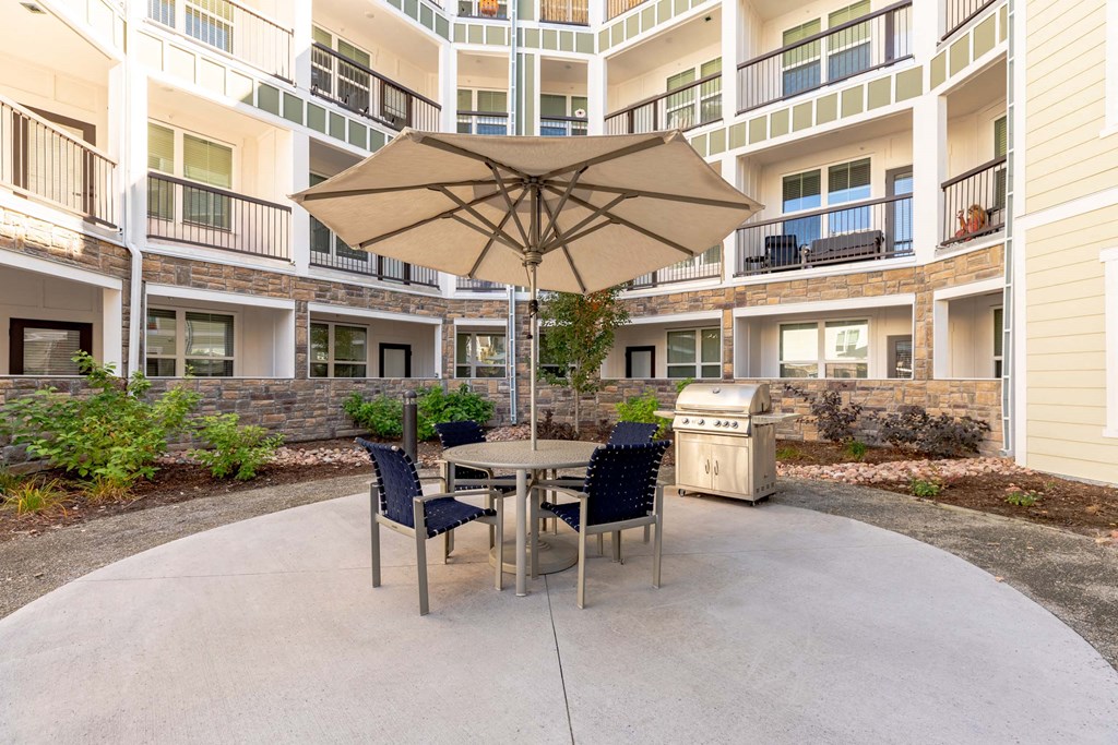 A patio with a table and chairs and an umbrella in front of apartment buildings.