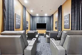 A home theater with grey seats and a black screen.