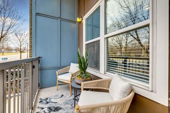A balcony with a table, chairs, and a potted plant.
