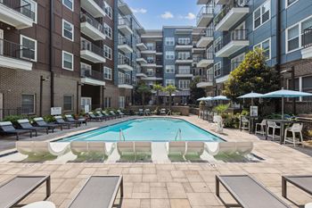 A swimming pool surrounded by lounge chairs and umbrellas in front of apartment buildings.