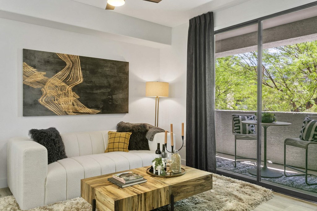 A modern living room with a white sofa, a wooden coffee table, and a large painting on the wall.