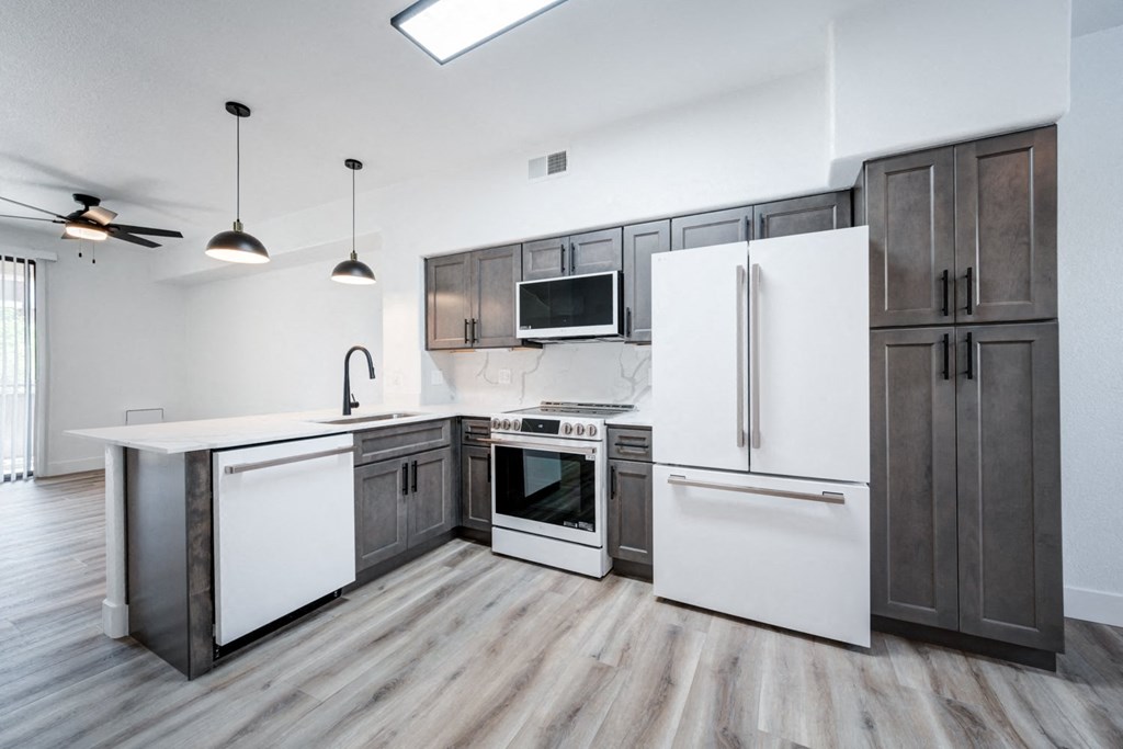A modern kitchen with a white refrigerator, wooden floors, and dark brown cabinets.