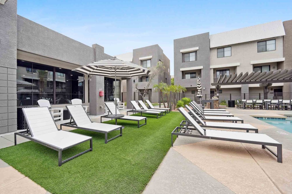 A row of sun loungers are on a lawn in front of a building.